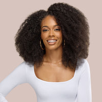 A stunning woman with voluminous, luxury textured hair extensions poses elegantly, showcasing the beauty and fullness of her natural curls. Her hair cascades effortlessly, exuding a radiant, healthy shine, perfectly complementing her confident expression. The soft, neutral background enhances the richness of her textured extensions, making them the focal point of the image—ideal for those seeking premium-quality hair solutions.