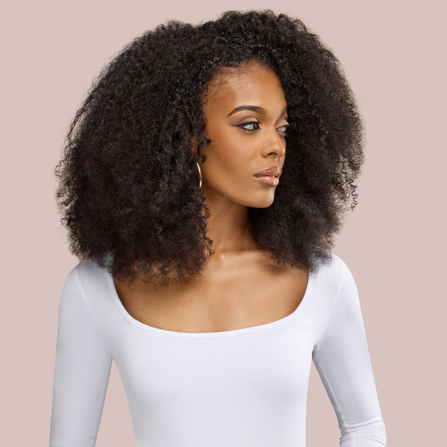 A stunning woman flaunts her voluminous afro kinky curly textured hair extensions, highlighting the natural beauty of tight, coily curls. The premier textured hair extensions seamlessly blend, creating a full-bodied and defined look. Her radiant expression and confident pose complement the luxurious texture of the curls, making the hairstyle stand out against the neutral background.