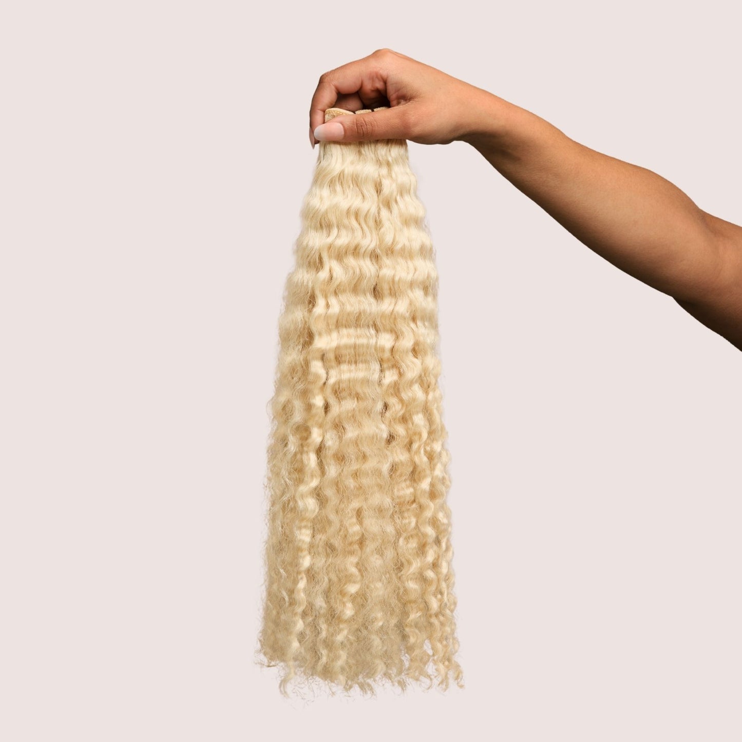 A hand holding a bundle of natural curly hair extensions in a radiant 613 blonde shade. The well-defined curls are soft and bouncy, cascading naturally with warm golden tones that add brightness and dimension. These luxury textured hair extensions provide an effortless blend with natural curly hair, offering enhanced length, volume, and versatility for protective styling.