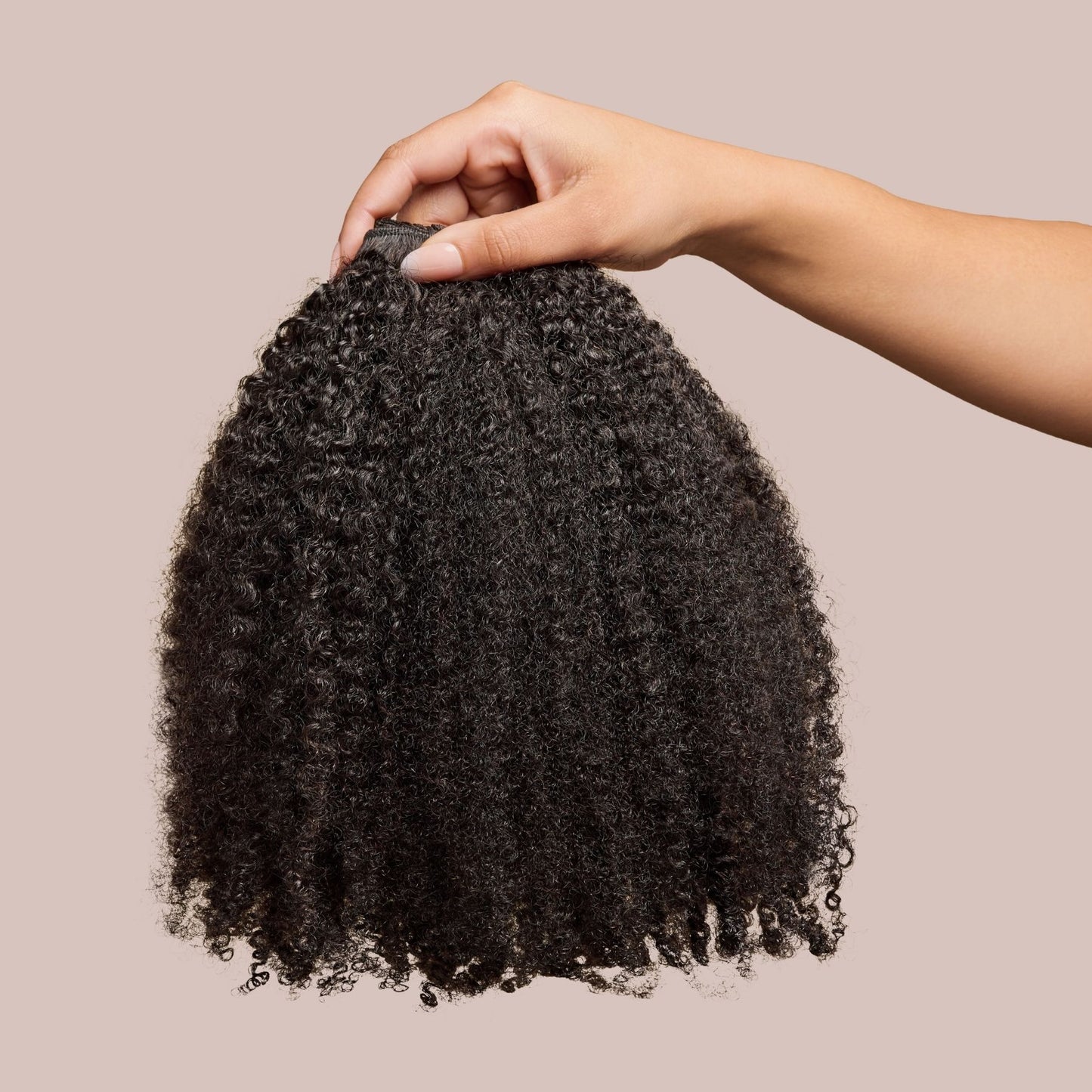 A hand delicately holding a bundle of Afro kinky curly hair extensions, showcasing the rich texture and natural volume of premium natural hair extensions. The deep black curls are tightly coiled, mimicking the look of natural 4B and 4C hair, making these luxury textured extensions a perfect match for protective styling and added fullness