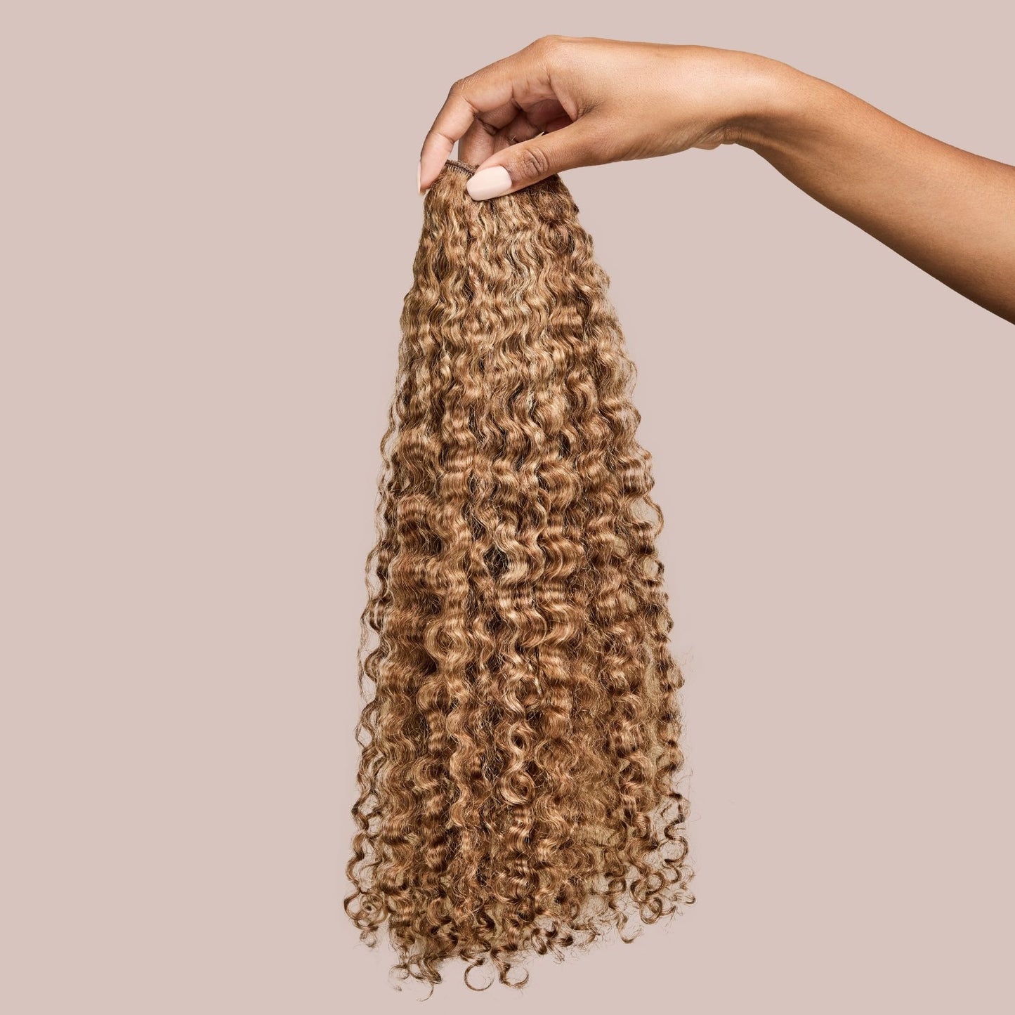A hand holding a bundle of natural curly hair extensions in a warm caramel shade. The soft, well-defined curls cascade with a natural bounce, showcasing rich golden-brown tones that add depth and dimension. These luxury textured hair extensions provide a voluminous and lightweight styling option, perfect for seamlessly blending with natural curly hair while enhancing length and fullness.