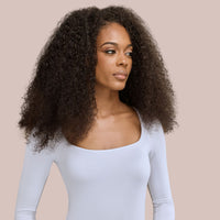 A stunning Black woman with voluminous luxury textured hair extensions styled in soft, defined curls. Her radiant smile and confident pose highlight the natural movement and fullness of the hair extensions, seamlessly blending with her natural hair. These high-quality hair extensions for Black women provide length, volume, and versatility, making them an excellent choice for protective styling and elegant, everyday looks.