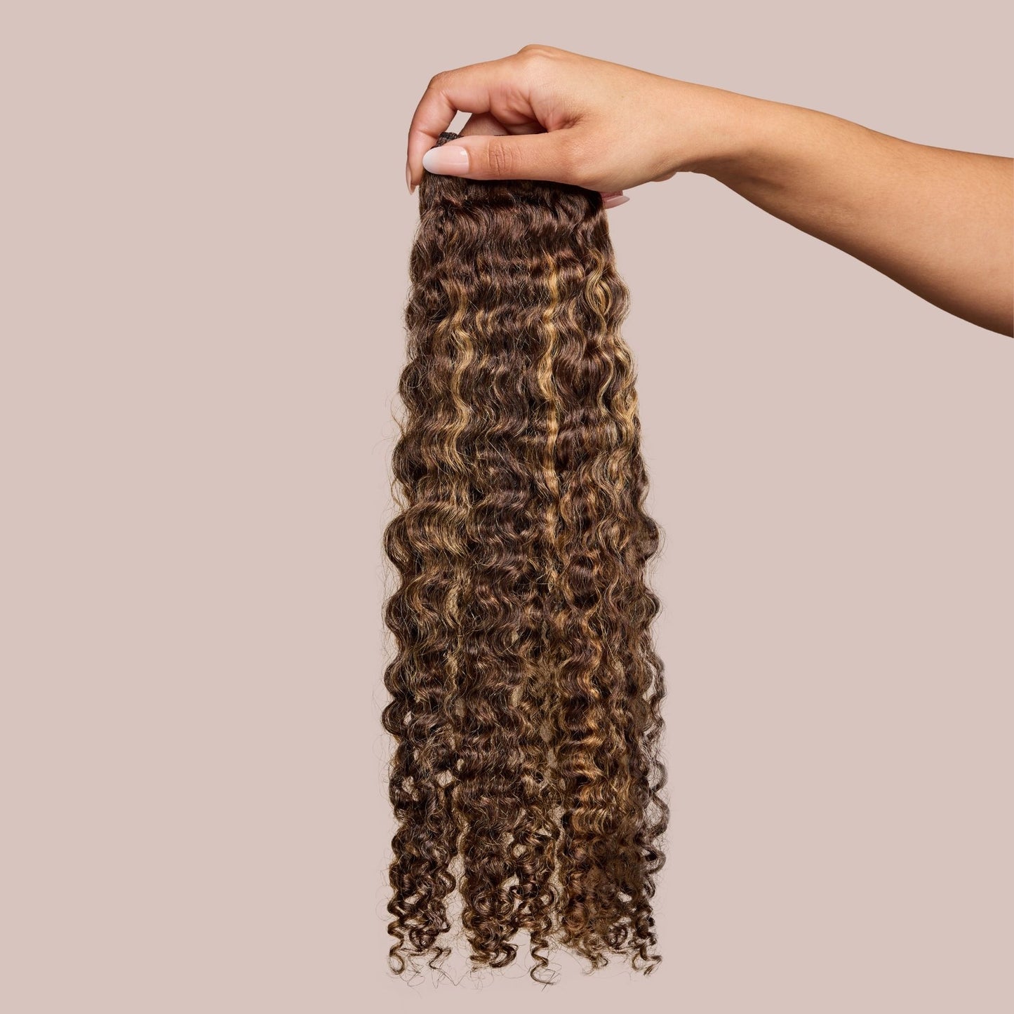 A hand gracefully holding a bundle of luxury textured hair extensions featuring soft, defined curls in a mix of deep brown and golden blonde highlights. These high-quality extensions have a natural luster and voluminous texture, ideal for enhancing curly and wavy hairstyles with added length and fullness.