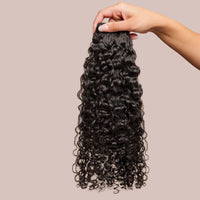 A close-up image of natural curly hair extensions with voluminous, well-defined curls in a deep, natural black shade. The luxurious texture showcases soft, bouncy ringlets that mimic the look of naturally curly hair, offering a full-bodied and lightweight appearance. These luxury textured hair extensions provide a seamless blend for those looking to enhance their natural curl pattern while adding length and volume.