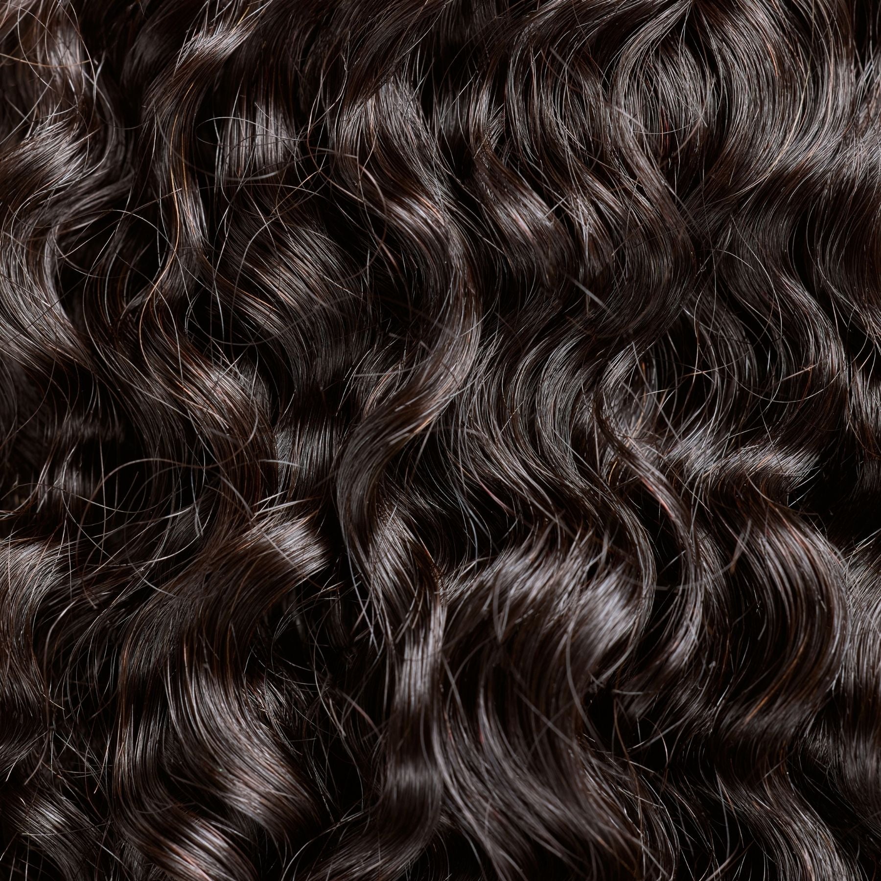 A close-up of natural curly hair extensions in a natural black shade, featuring soft, defined curls that add volume and movement. These luxury textured hair extensions mimic the look of naturally curly hair, offering a lightweight feel and a seamless blend with natural textures. The high-quality strands provide a bouncy, full-bodied appearance with a healthy shine, perfect for creating effortlessly glamorous styles.