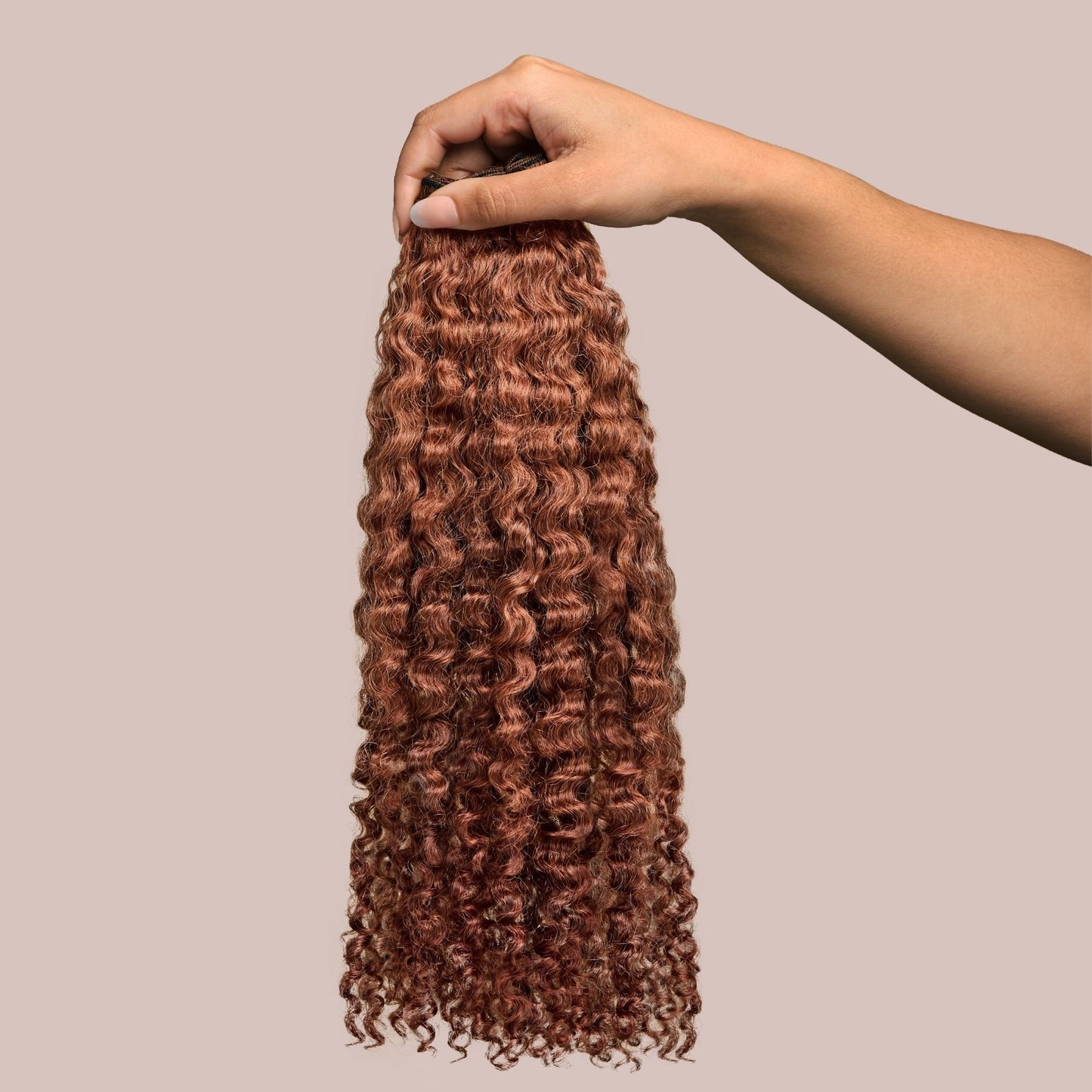 A hand holding a bundle of kinky curly textured hair extensions in a rich auburn shade. The tight, springy curls are soft, voluminous, and well-defined, with warm reddish-brown tones that add depth and vibrancy. These premier textured hair extensions offer a full-bodied, bouncy appearance, perfect for adding length, volume, and versatility to protective styles while maintaining a natural, seamless blend.