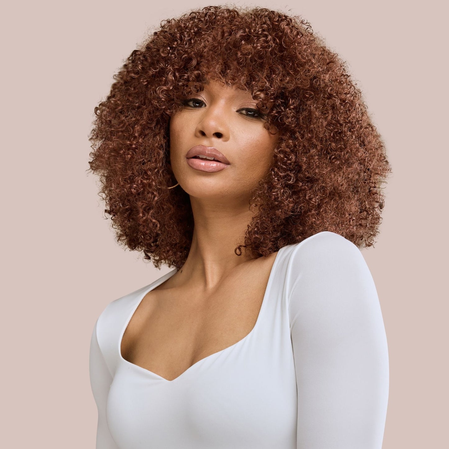 A confident woman showcasing voluminous kinky curly textured hair extensions in a rich auburn shade. Her defined, springy curls frame her face beautifully, with warm reddish-brown tones adding depth and vibrancy. These premier textured hair extensions blend seamlessly with natural curls, offering an elegant and versatile styling option for enhanced length, volume, and dimension.