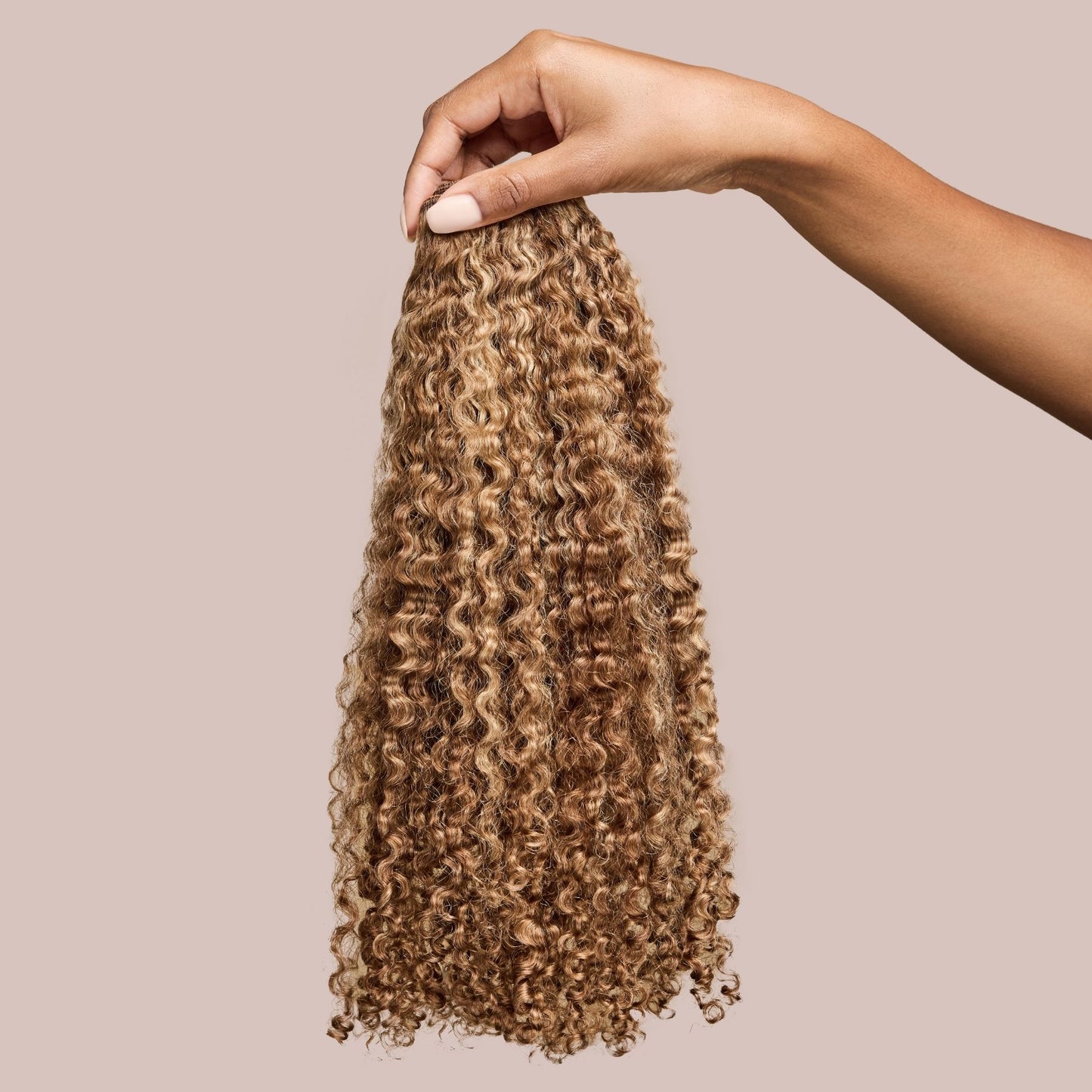 A hand holding a bundle of natural curly hair extensions in a stunning golden espresso shade. The well-defined curls are soft and bouncy, cascading naturally with deep brown tones infused with warm golden highlights, adding richness and dimension. These luxury textured hair extensions provide an effortless blend with natural curly hair, offering enhanced length, volume, and versatility for protective styling.