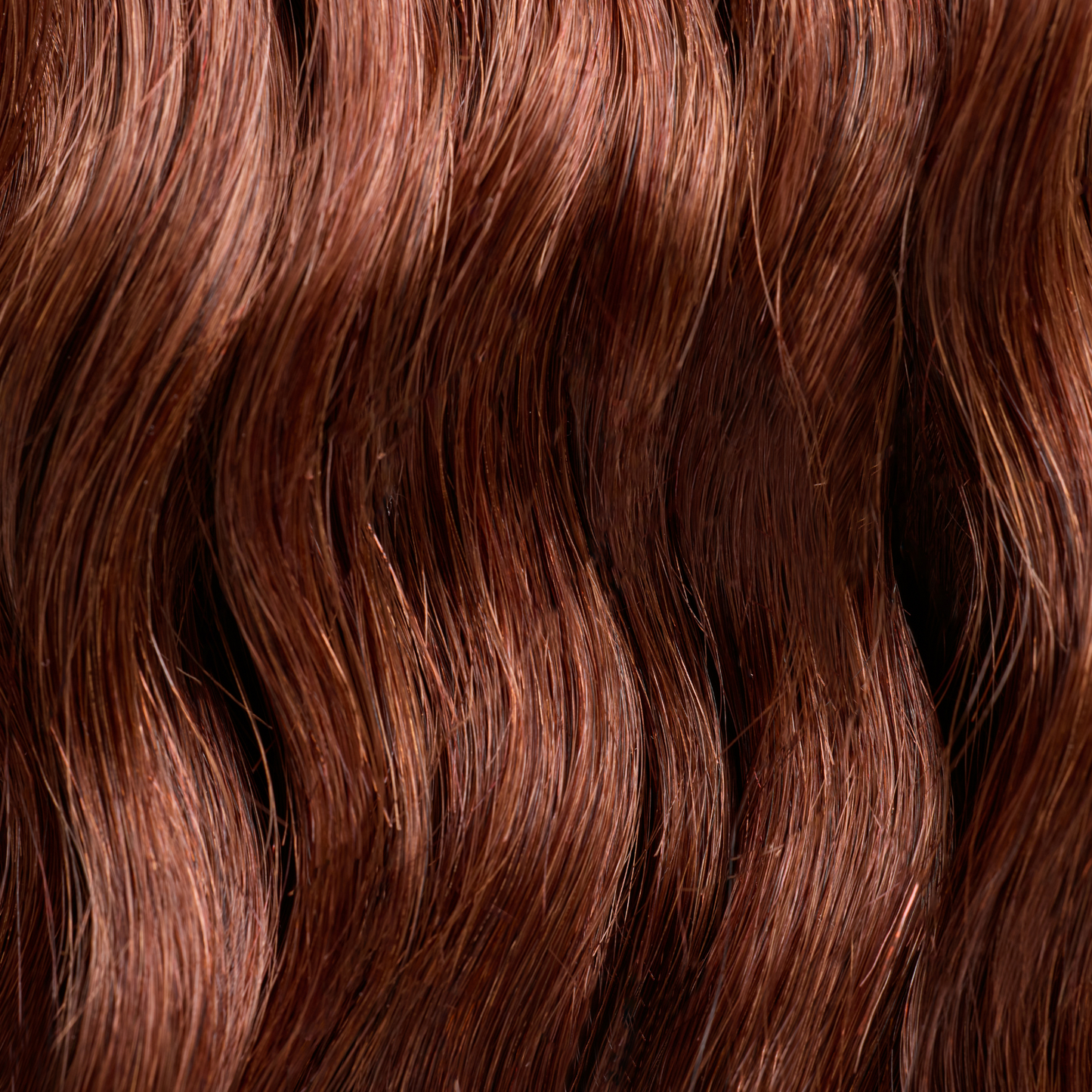 A close-up of loose wavy textured hair extensions in a rich auburn shade, featuring soft, flowing waves that enhance natural volume and movement. These premier textured hair extensions have a silky, lightweight feel with a radiant shine, providing a seamless blend with natural hair. The high-quality strands offer versatility for styling, making them perfect for achieving an effortlessly glamorous and voluminous look.