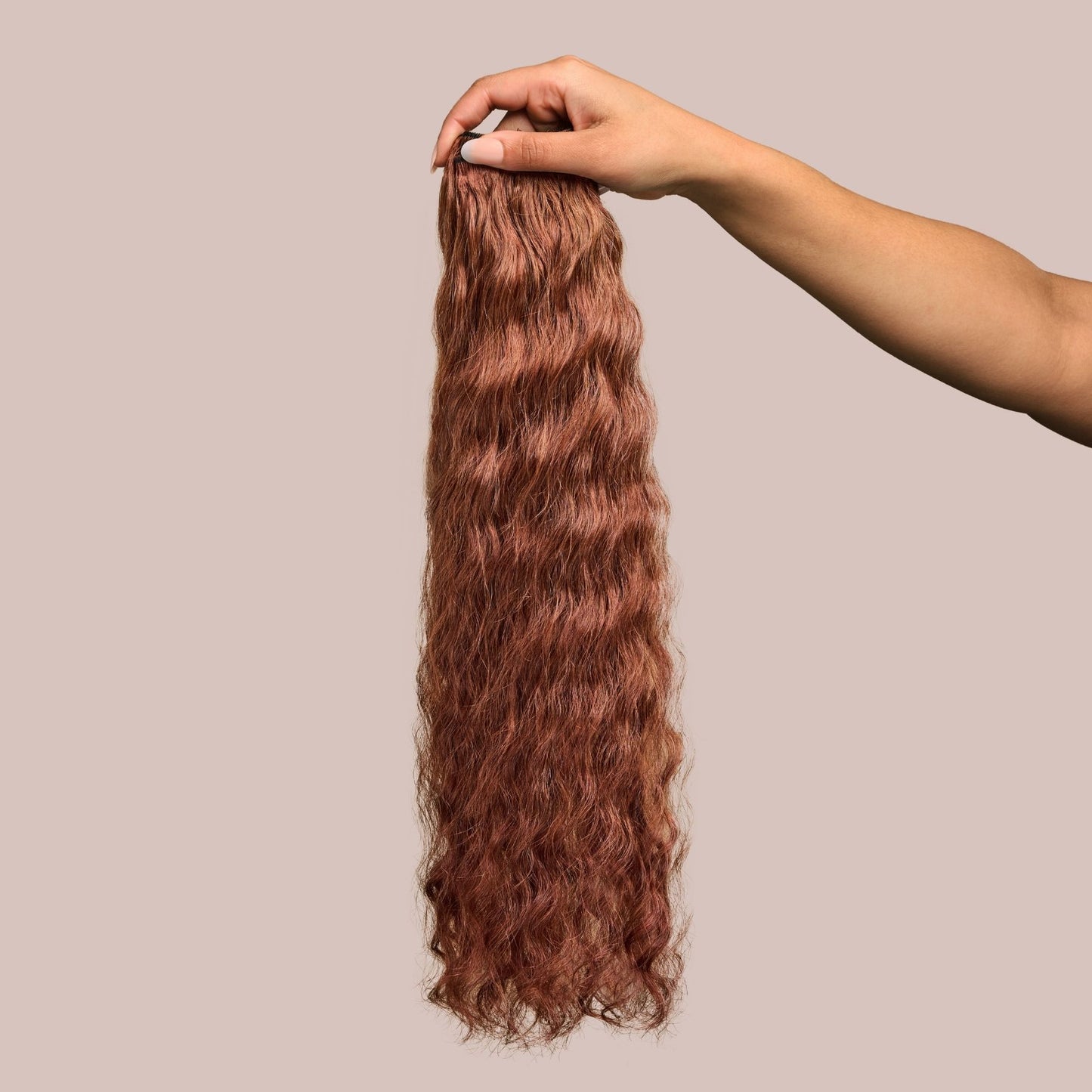 A hand holding a bundle of loose wavy textured hair extensions in a rich auburn shade. The soft, flowing waves have a silky texture with warm reddish-brown tones, adding depth and dimension for a naturally vibrant look. These premier textured hair extensions provide versatility for styling, making them an excellent choice for adding length, fullness, and a seamless blend with natural hair.