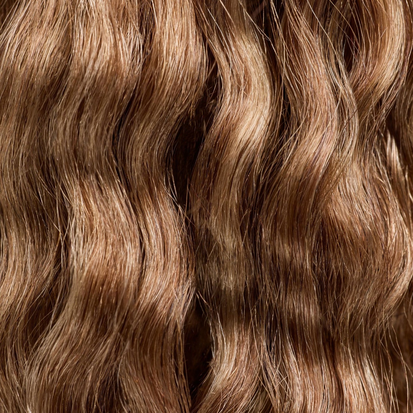 A close-up image of loose wavy textured hair extensions in a rich caramel shade. The soft, flowing waves feature warm golden-brown tones, adding depth and dimension for a naturally radiant look. These premier textured hair extensions provide effortless volume and length, making them a perfect choice for those seeking a seamless blend with natural hair while enhancing their style with a smooth, wavy texture.