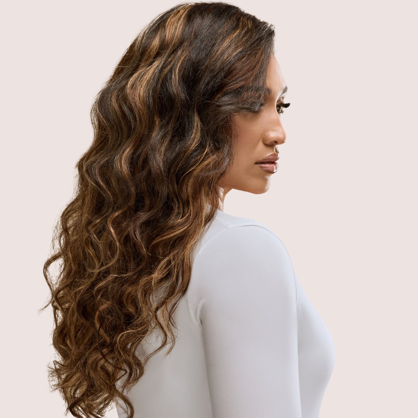 A stunning woman with flowing loose wavy textured hair extensions in a rich caramel brown shade. Her well-defined waves cascade effortlessly, with warm golden-brown tones adding depth and dimension. These premier textured hair extensions provide natural movement, added length, and luxurious fullness, offering a seamless blend for an elegant and sophisticated look.