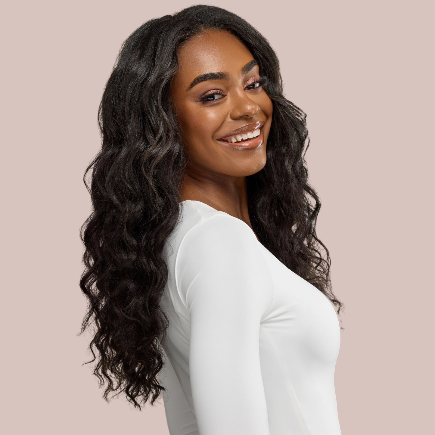 A stunning black woman with long, flowing loose wavy textured hair extensions showcases the luxurious volume and natural movement of premier textured hair extensions. Her soft, bouncy waves cascade effortlessly over her shoulders, enhancing her radiant beauty. The seamless blend of the extensions creates a flawless, full-bodied look, perfect for those seeking natural yet glamorous waves.