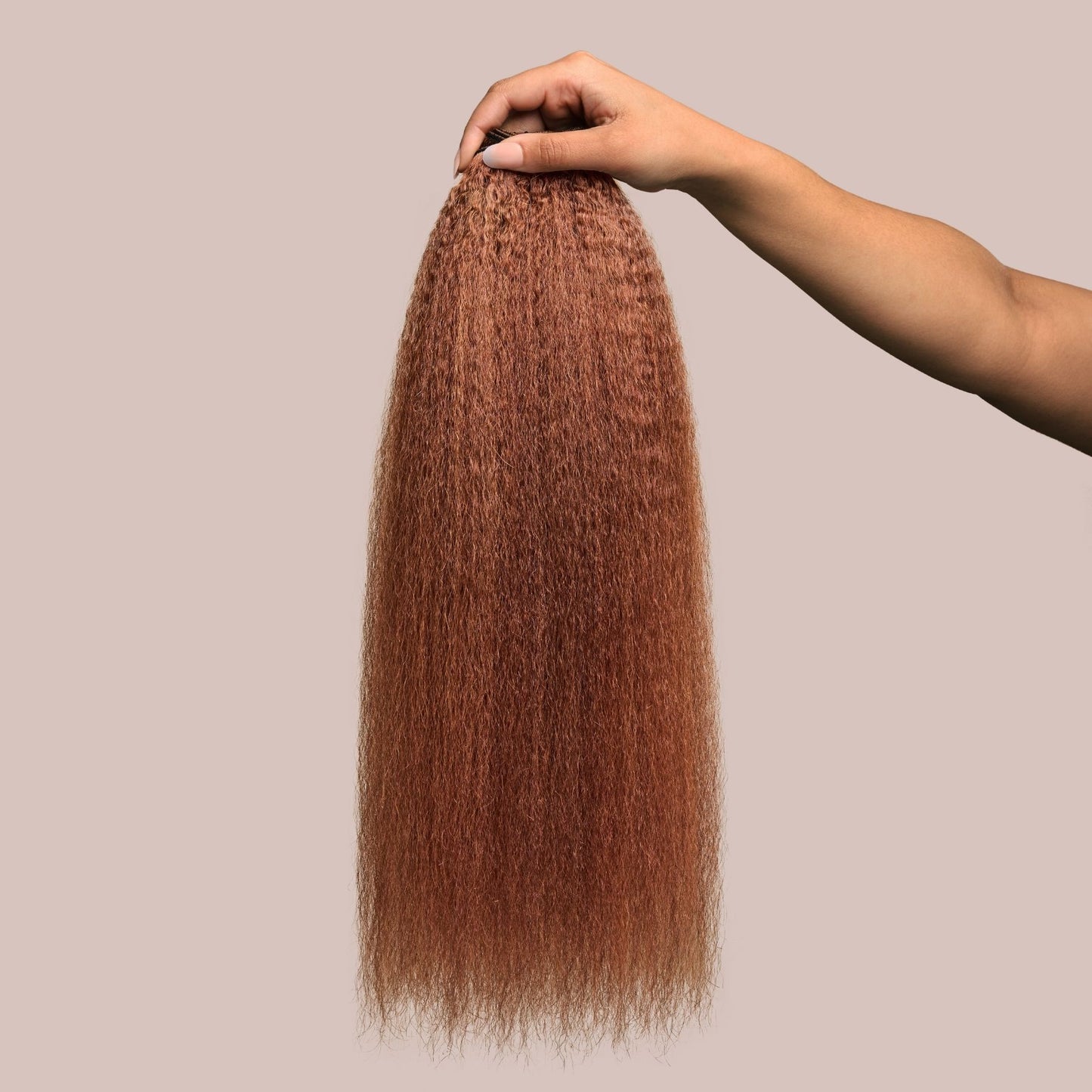 A hand holding a bundle of kinky straight textured hair extensions in a rich auburn shade. The thick, voluminous strands have a soft, blown-out appearance, with warm reddish-brown tones that add depth and vibrancy. These luxury textured hair extensions offer versatility, fullness, and a seamless blend, making them a perfect choice for protective styling and natural-looking volume.
