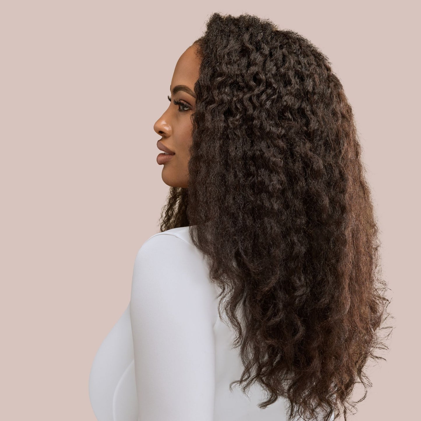 A confident woman with voluminous kinky straight textured hair extensions in a rich, natural finish. Her sleek, blown-out strands mimic the look of gently straightened African American hair, adding fullness and movement. Styled with elegance, she showcases professional hair extensions that seamlessly blend with natural textures, offering length, volume, and versatility for protective styling.