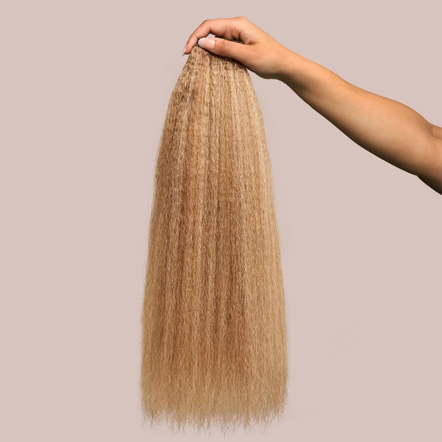A hand holding a bundle of kinky straight hair extensions in a warm caramel shade. The thick, textured strands have a soft, blown-out appearance, showcasing rich golden-brown tones that add warmth and dimension. These luxury textured hair extensions provide volume, versatility, and a seamless blend for protective styling, making them an excellent choice for a natural yet polished look.